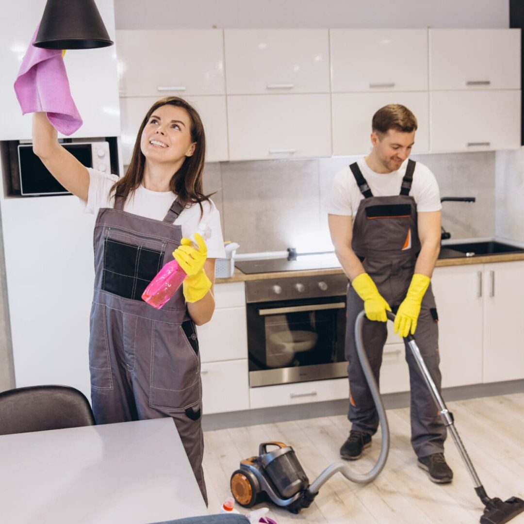 Cleaning company workers cleaning a kitchen using a vacuum cleaner and a spray detergent Two people cleaning a modern kitchen.